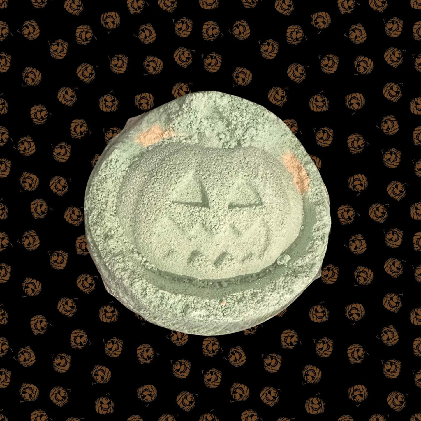 Green and orange pumpkin bath bomb on a Halloween-themed background