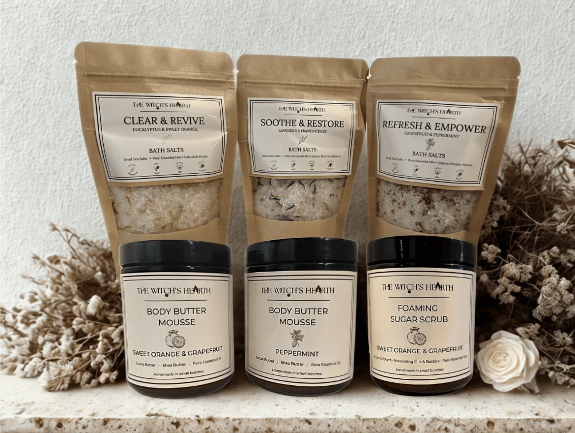 Set of skincare products including bath salts, body butter mousse, and foaming sugar scrub with labels on a neutral background.