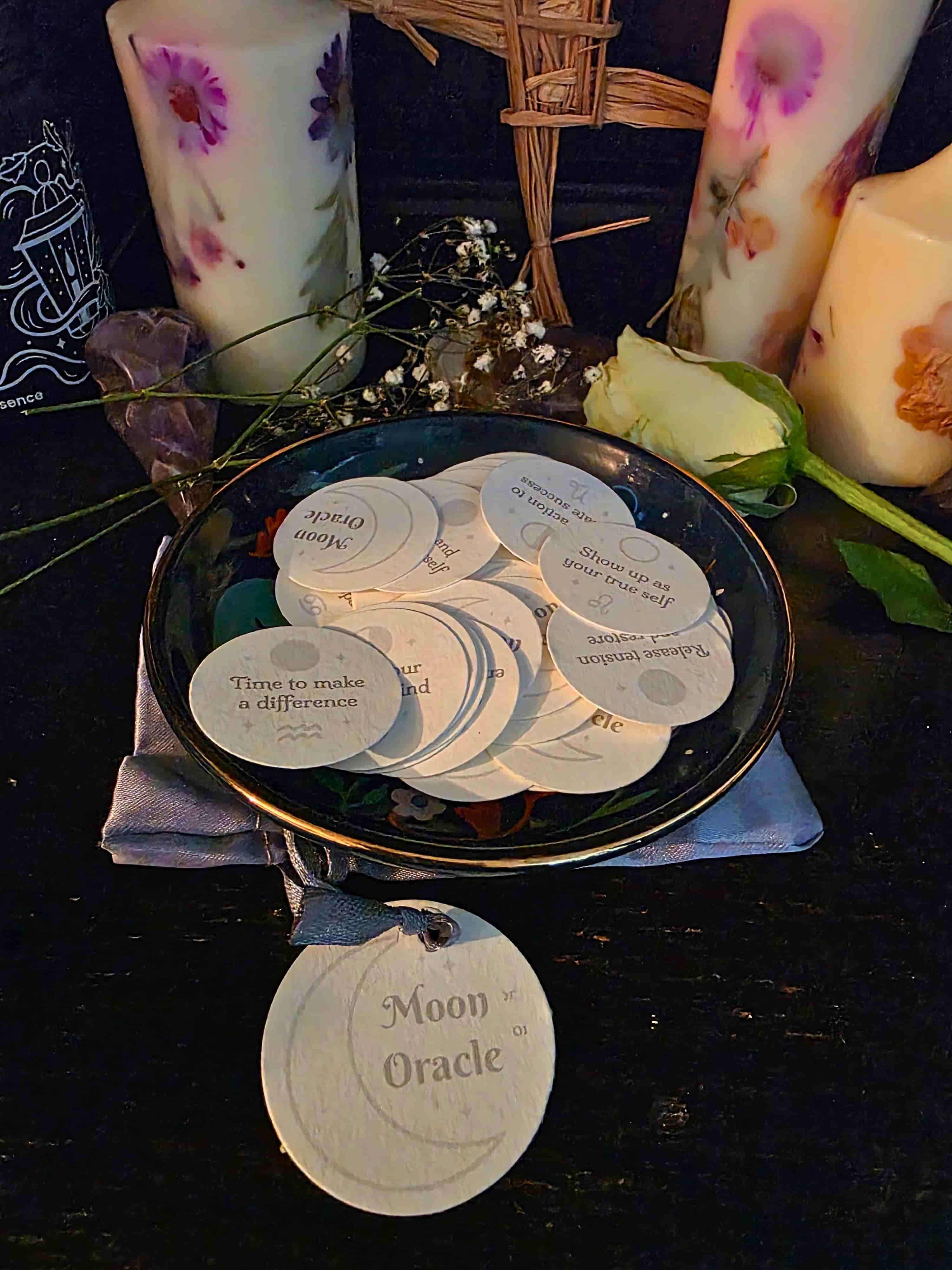 Set of 'Moon Oracle' cards on a dark surface with candles and flowers.