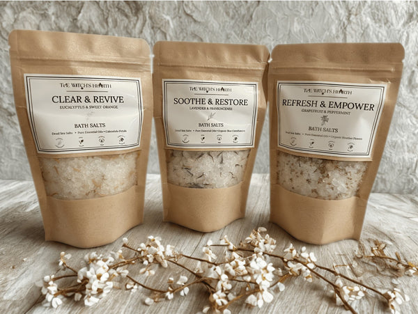 Three packages of bath salts with labels on a textured surface with decorative branches.