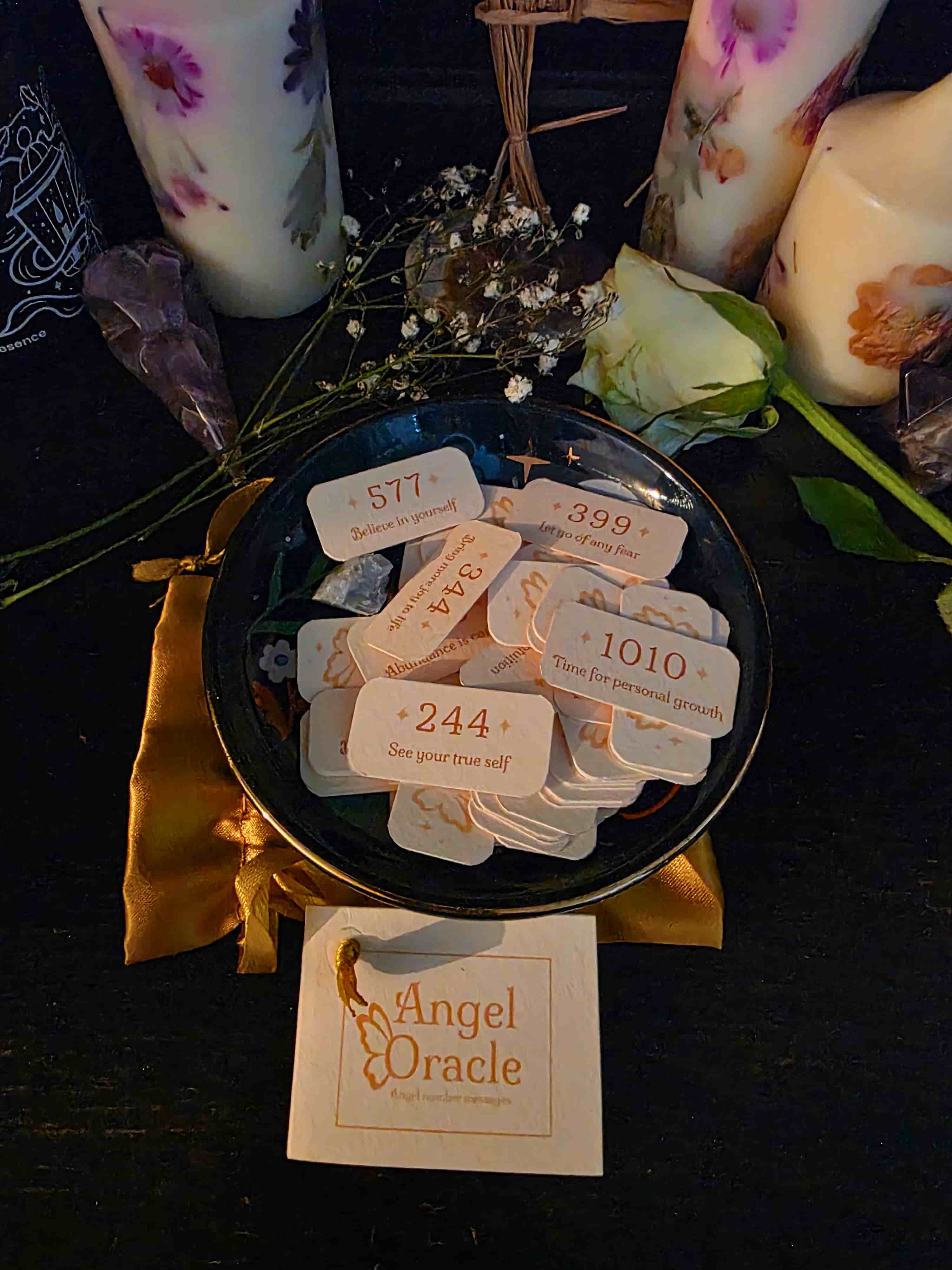 Set of angel oracle cards with a black dish, candles, and flowers on a dark surface.
