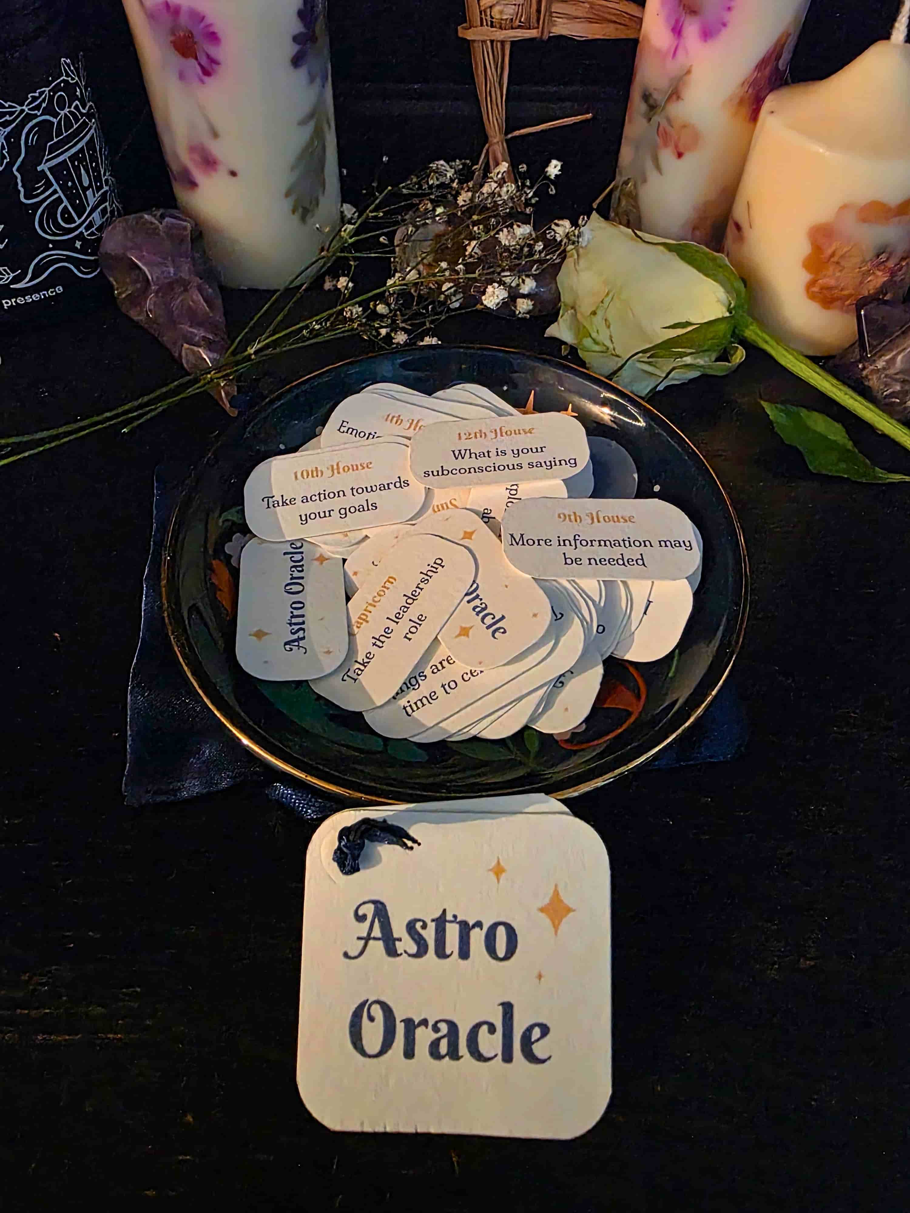 Astro Oracle cards on a dark surface with candles and flowers in the background